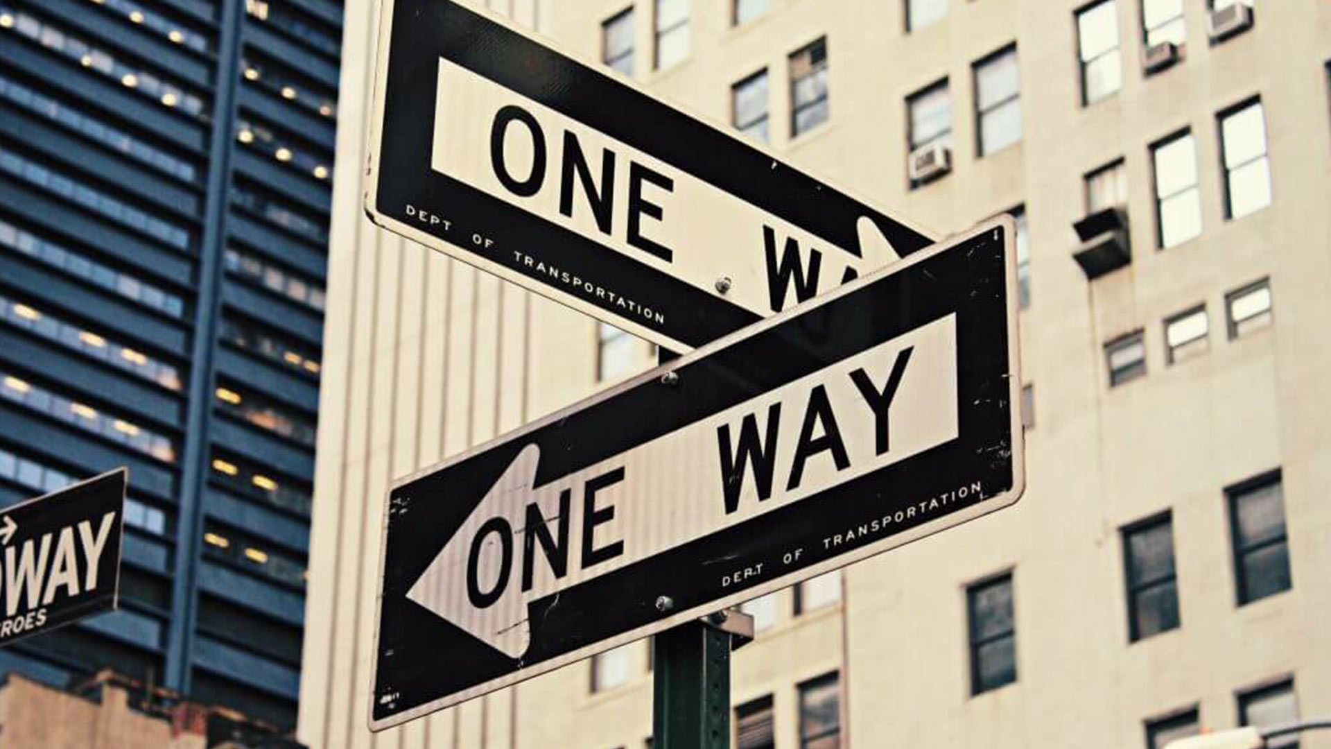 a pair of black one way street signs pointing in a city