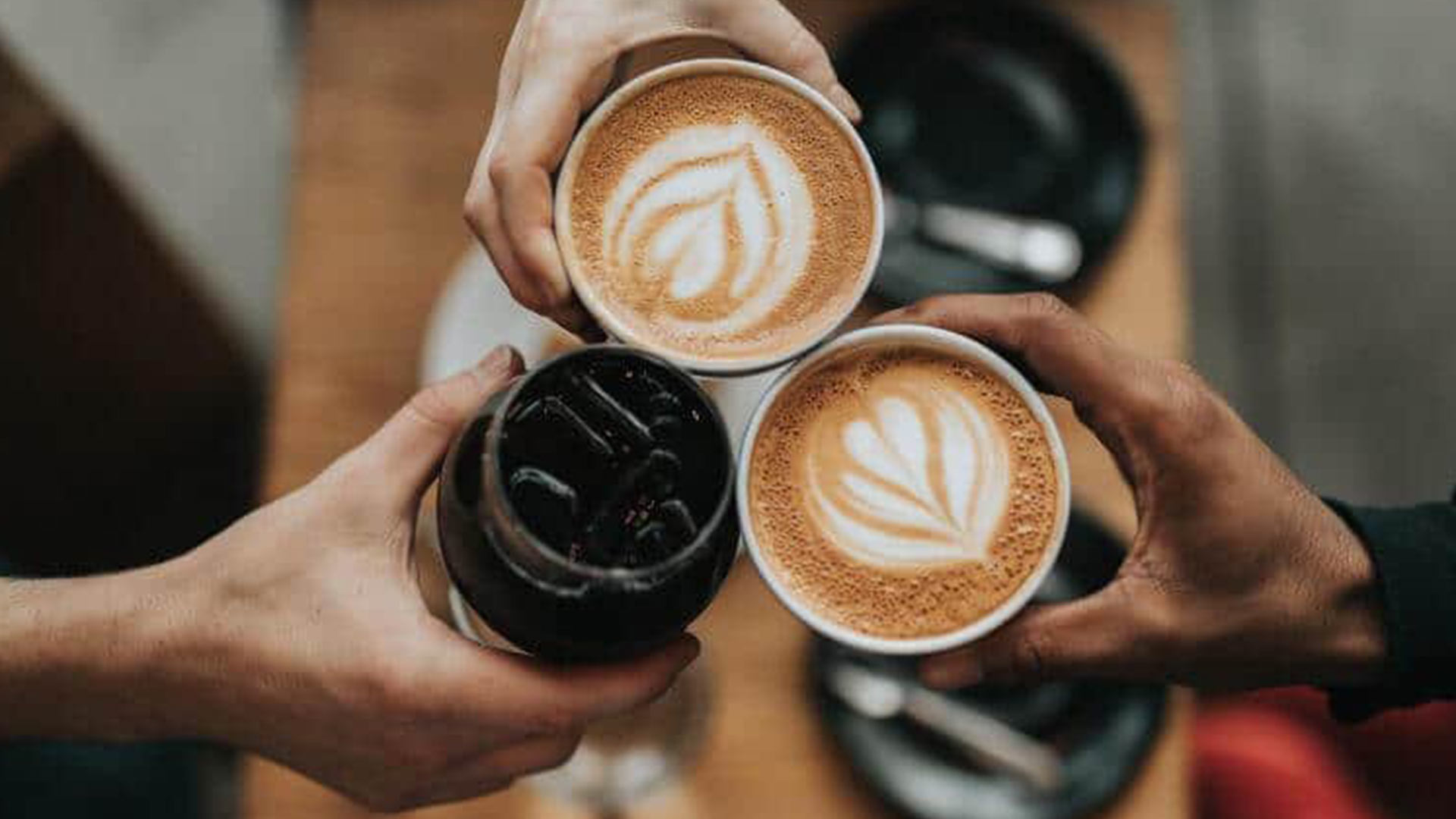 aerial shot of three friend's hands clinking coffee glasses together in a coffee shot