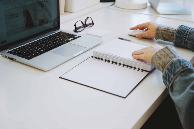 Person sitting at a desk with a notebook and laptop
