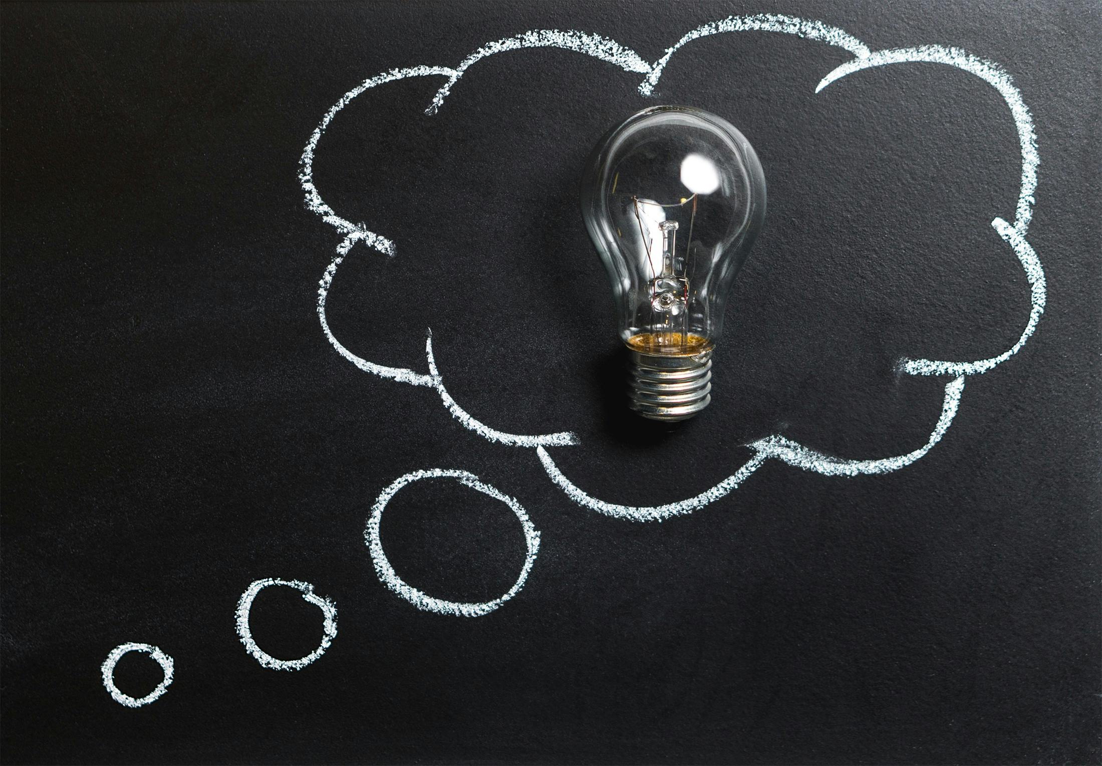 idea lightbulb on a black chalkboard with chalk thought bubble